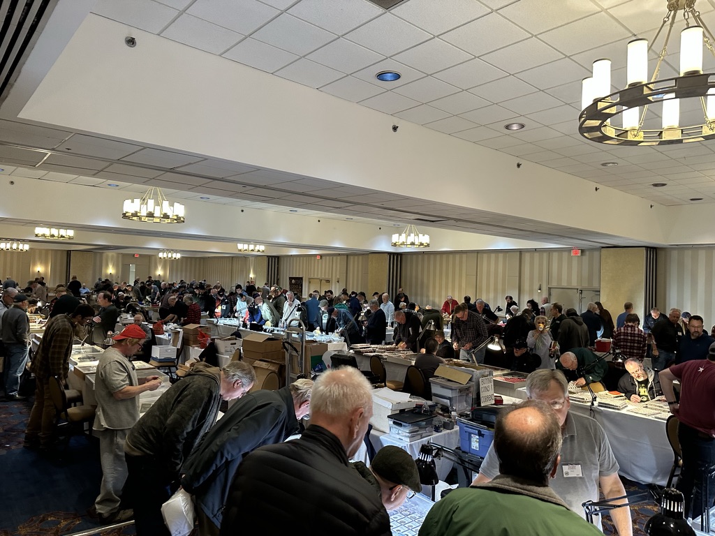 Dealers and visitors seated at tables during a coin show.